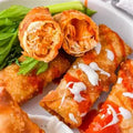 Close-up of buffalo chicken spring rolls on a white plate, garnished with celery and a drizzle of white sauce.